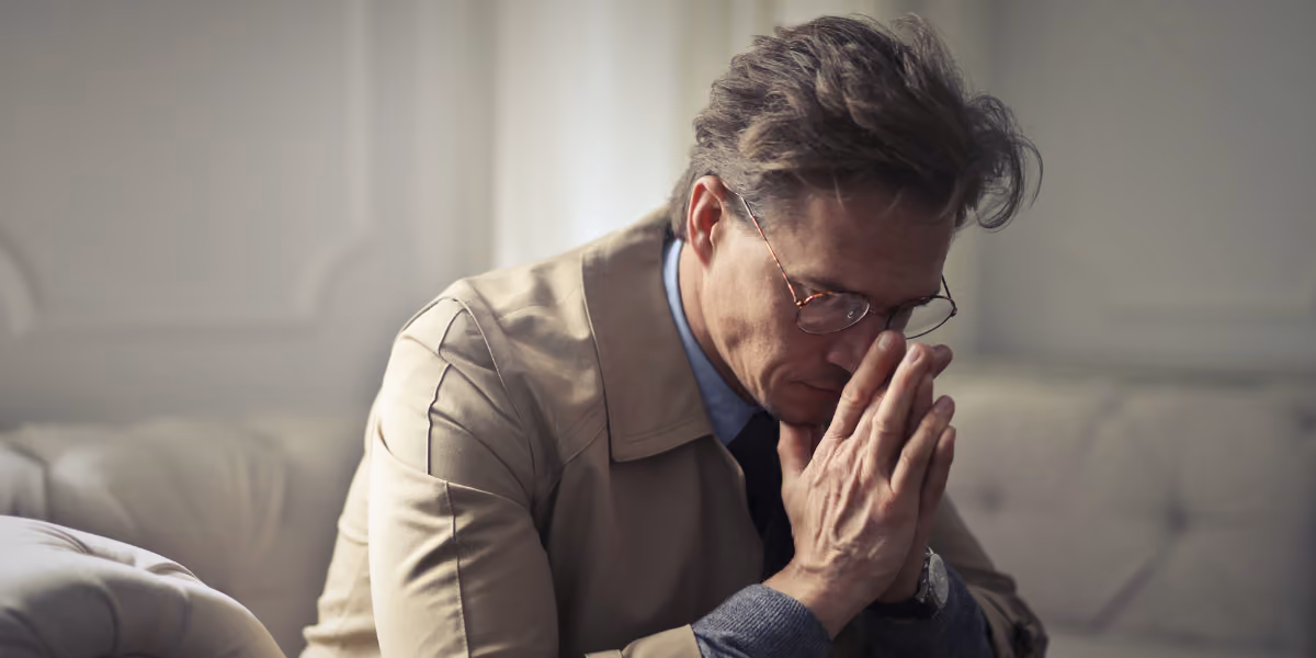 A stressed man sitting with his hands held in a prayer position close to his face.